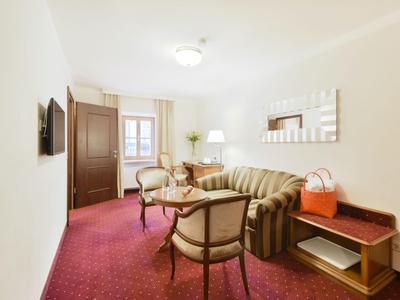 Jasny pokój hotelowy z czerwonym dywanem, sofą, fotelami i drewnianymi meblami.