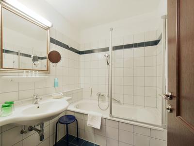 Mała łazienka z wanną, parawanem prysznicowym, umywalką i lustrem w pokoju hotelowym.