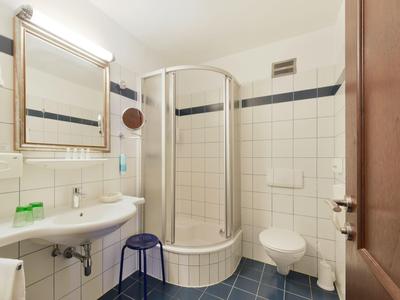 Mała łazienka z okrągłą prysznicem, umywalką, toaletą i niebieską, kafelkowaną podłogą.