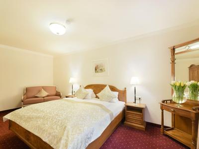 Jasny pokój hotelowy z podwójnym łóżkiem, stolikami nocnymi i lustrem z kwiatową dekoracją.