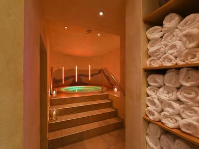 Vasca idromassaggio riscaldata con scalini e pila di asciugamani in una stanza illuminata caldamente.