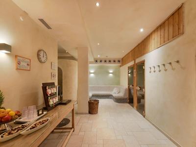 Corridoio luminoso con piastrelle chiare, panca, ciotola di frutta e ganci a muro in un hotel.