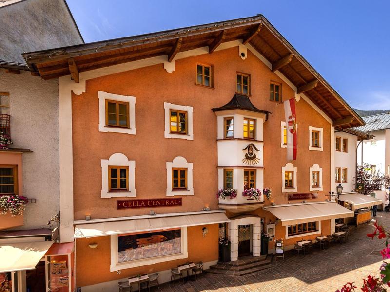 Edificio alberghiero tradizionale con facciata arancione e decorazioni floreali sui davanzali in vicolo soleggiato.