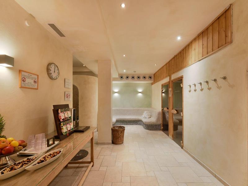 Corridoio luminoso con piastrelle chiare, panca, ciotola di frutta e ganci a muro in un hotel.