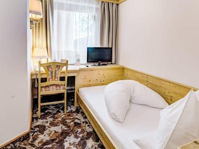 Kleine hotelkamer met eenpersoonsbed, bureau en raam met gordijnen.