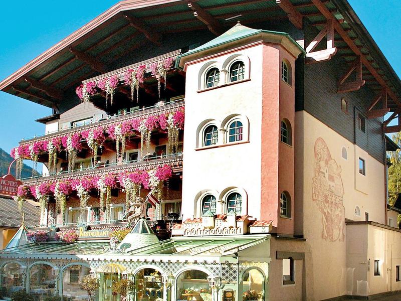 Sfeervol hotel met bloemrijke balkons en een traditioneel alpien ontwerp onder een heldere lucht.