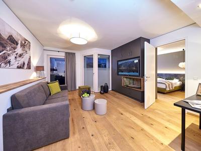 Moderně zařízený obývací pokoj se šedou pohovkou, dřevěnou podlahou a krbem v hotelovém pokoji.