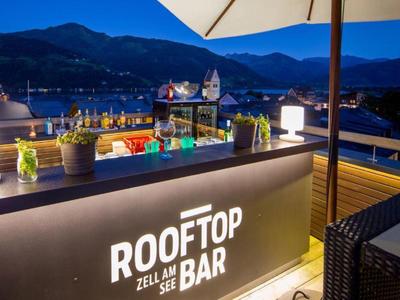 Večerní pohled na osvětlený bar na střeše s horami v pozadí