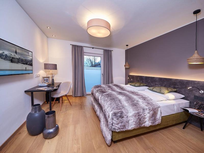 Moderně zařízená ložnice s manželskou postelí, psacím stolem a oknem s závěsy.