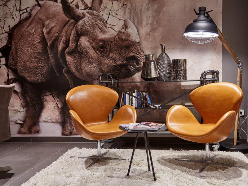 Pohodlný prostor k sezení se dvěma oranžovými křesly a stolem před stěnou s malbou nosorožce.