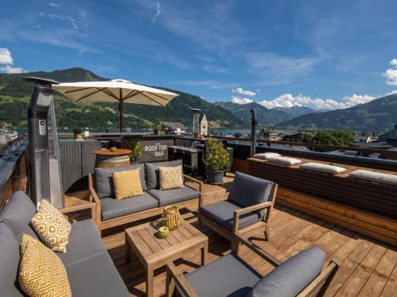 Střešní terasa s odpočinkovým nábytkem a výhledem na hory za slunečného dne.