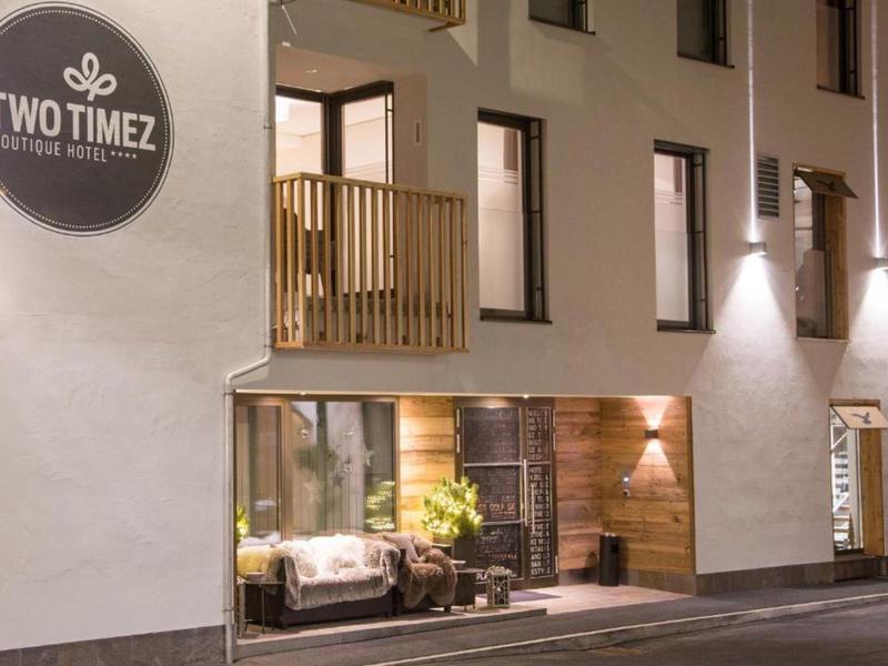 Moderní hotelová fasáda s osvětleným balkonem a útulným posezením v přízemí.