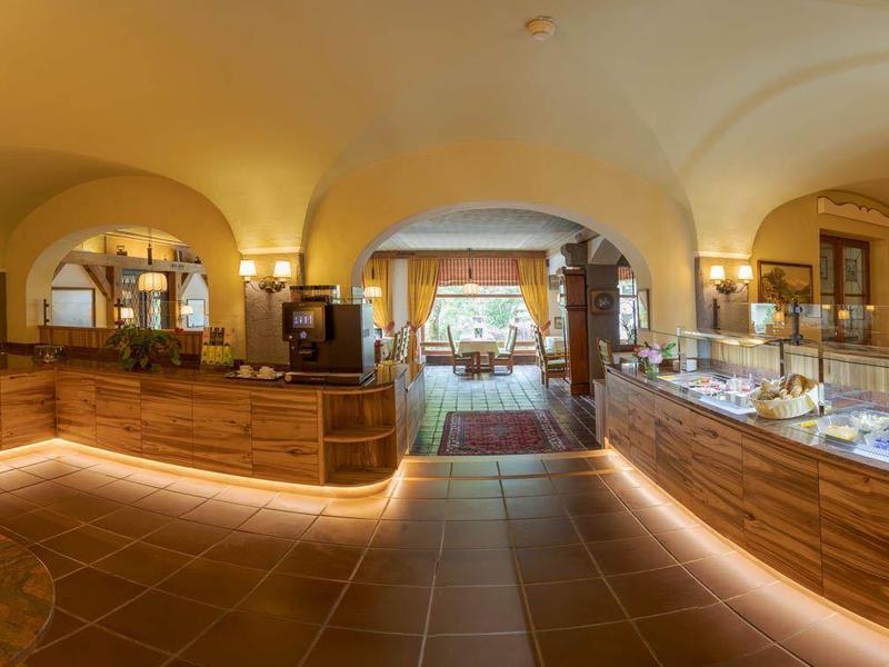 Accogliente hall d'albergo con banco in legno, composizioni floreali e luce calda.