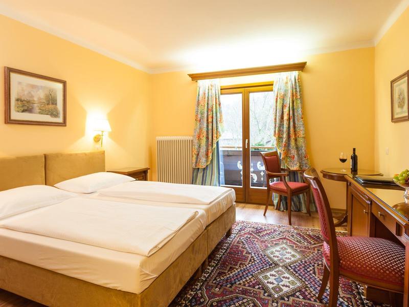 Camera d'hotel luminosa con letto matrimoniale, tappeto e balcone con vista esterna.