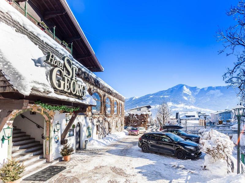 Hotel con ingresso innevato e parcheggio davanti a paesaggio montano sotto cielo sereno