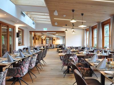 Geräumiger Speisesaal mit Holzdecke, großen Fenstern und elegant gedeckten Tischen.