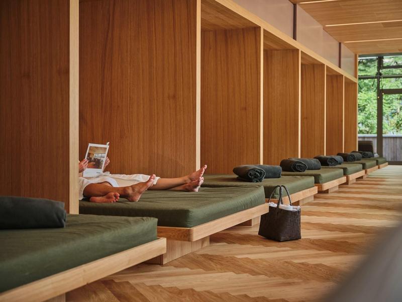 Ontspannen gast ligt op een lounge met groene kussens in een rustige ruimte met houten wanden.