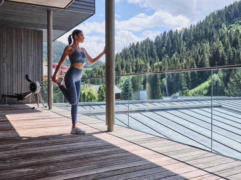 Vrouw die mediteert op terras met uitzicht op bos en bergen bij zonneschijn