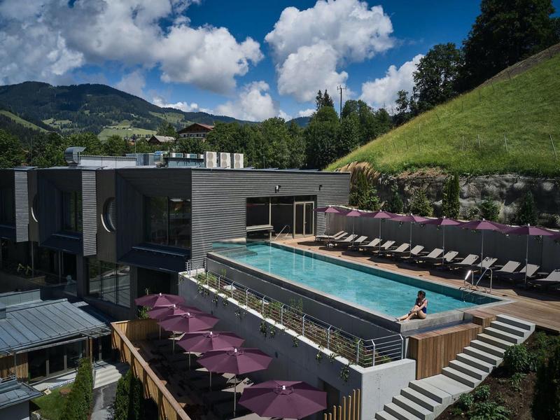 Modern zwembad met ligstoelen tegen heuvels en bewolkte lucht bij een hotel.