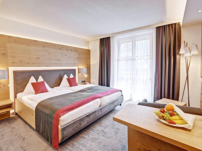 Modern ingerichte hotelkamer met tweepersoonsbed, groot raam en houten meubels.