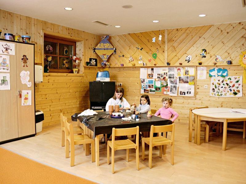 Kleuterklaslokaal met drie kinderen aan een tafel vol knutselmateriaal en kindvriendelijk meubilair.