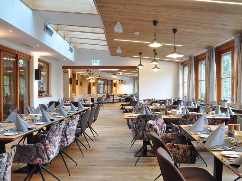 Modern eetzaal met houten vloer, veel tafels en grote ramen.