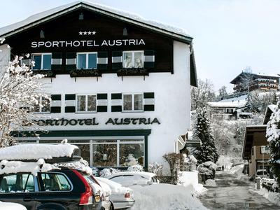 Sporthotel Austria cubierto de nieve con coches aparcados y paisaje invernal