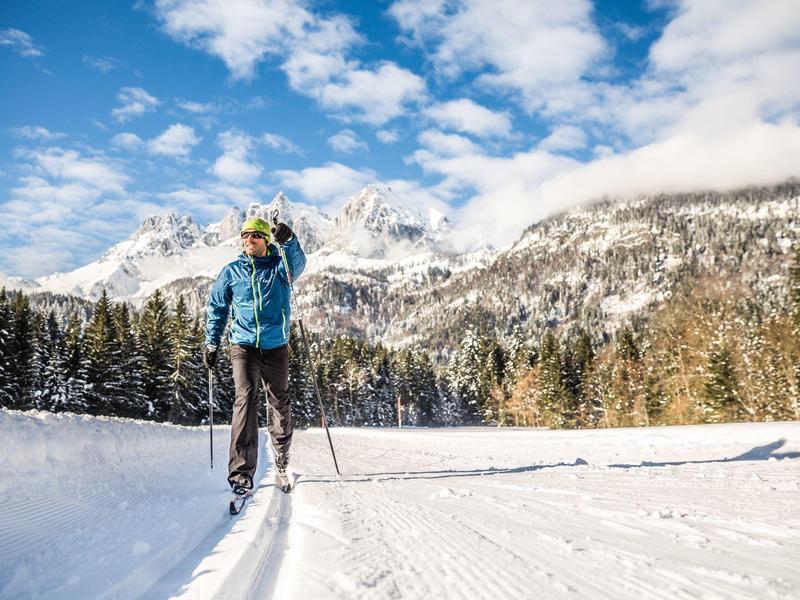 Persona con ropa de invierno en pista de esquí preparada frente a montañas nevadas.
