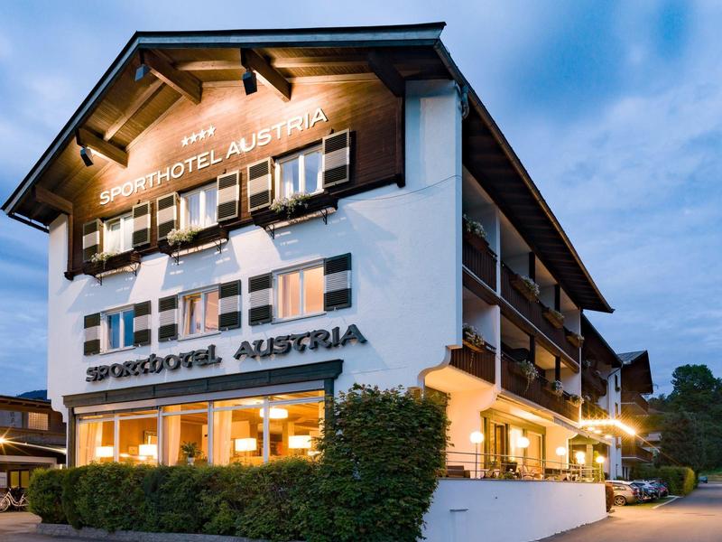 Edificio moderno de hotel con ventanas iluminadas al anochecer bajo un cielo azul.