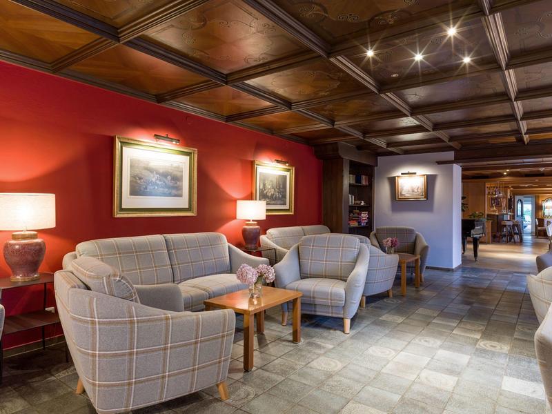 Sala de hotel con sillones y paredes rojas, iluminación cálida y techo de madera decorativo.