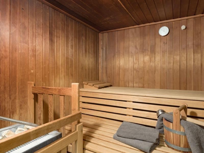 Sauna interior con paredes de madera, bancos de madera en varios niveles y balde de sauna con toallas.