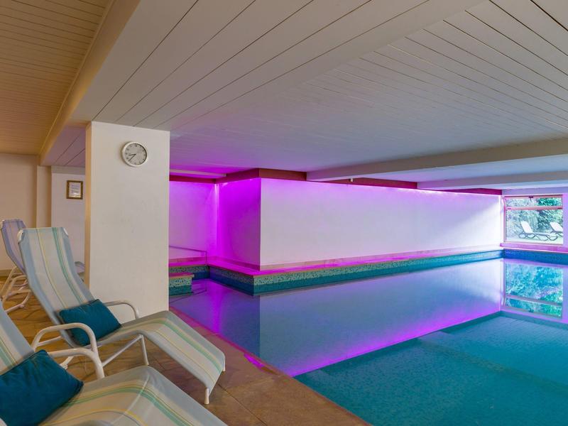 Área de piscina interior con tumbonas relajantes y luz ambiental en hotel.