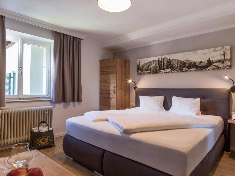 Habitación de hotel moderna con cama doble grande, iluminación suave y ventanas con cortinas opacas.