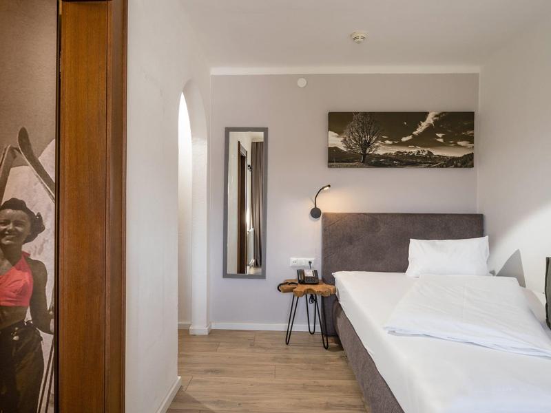 Habitación de hotel moderna con cama blanca, suelo de madera, mesa de noche y arte en la pared.