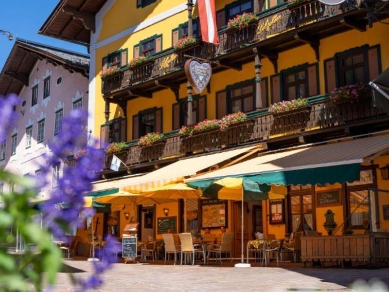 Bâtiment d'hôtel traditionnel avec balcon, ciel bleu et fleurs au premier plan.