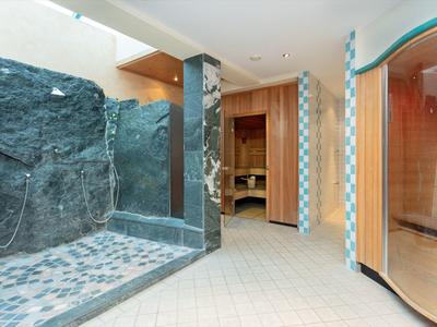 Moderní hotelové lázně s kamennou sprchou a saunou v světlé, čisté místnosti.