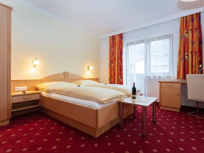 Cozy hotel room with double bed, wardrobe, table, and chair in front of window with curtains.