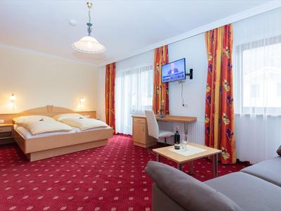 Bright hotel room with double bed, carpeted floor, sofa, desk, and wall-mounted TV.
