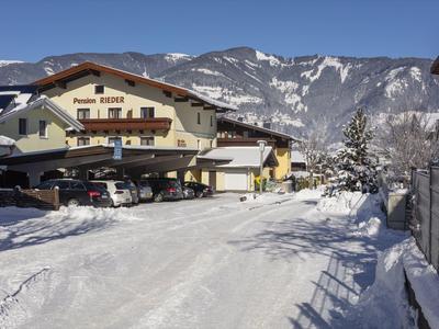 Hotelová budova pokrytá sněhem s horami v pozadí za jasné oblohy.