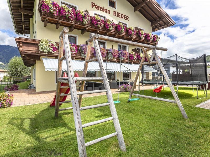 Dětské hřiště s houpačkou před hotelem s květinami na balkóně.