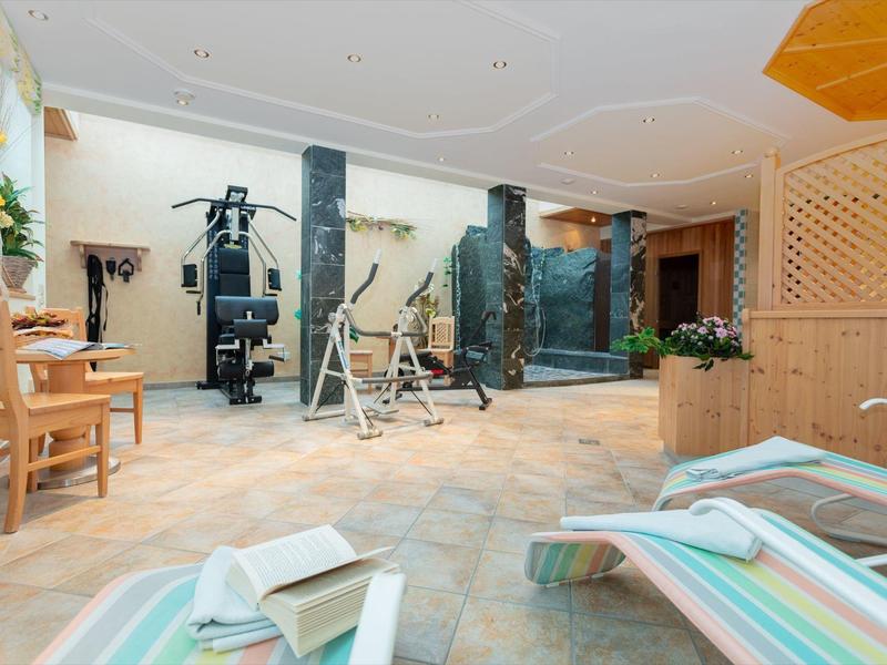 Jasně osvětlená posilovna s tréninkovými stroji a lehátky v popředí.