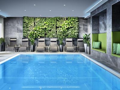 Nowoczesny basen kryty z zieloną ścianą, leżakami i przytulnymi wnękami.