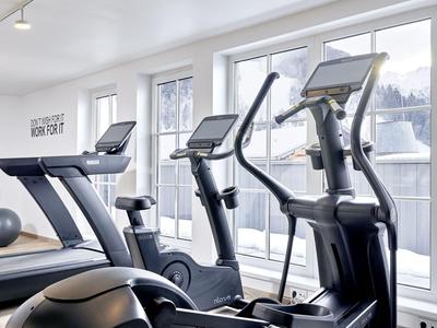 Palestra moderna con tapis roulant e cyclette davanti a grandi finestre con vista montagna.