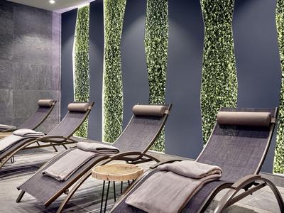 Nowoczesne leżaki z poduszkami i kocami przed dekoracyjną ścianą z zielonymi pionowymi pasami roślin.