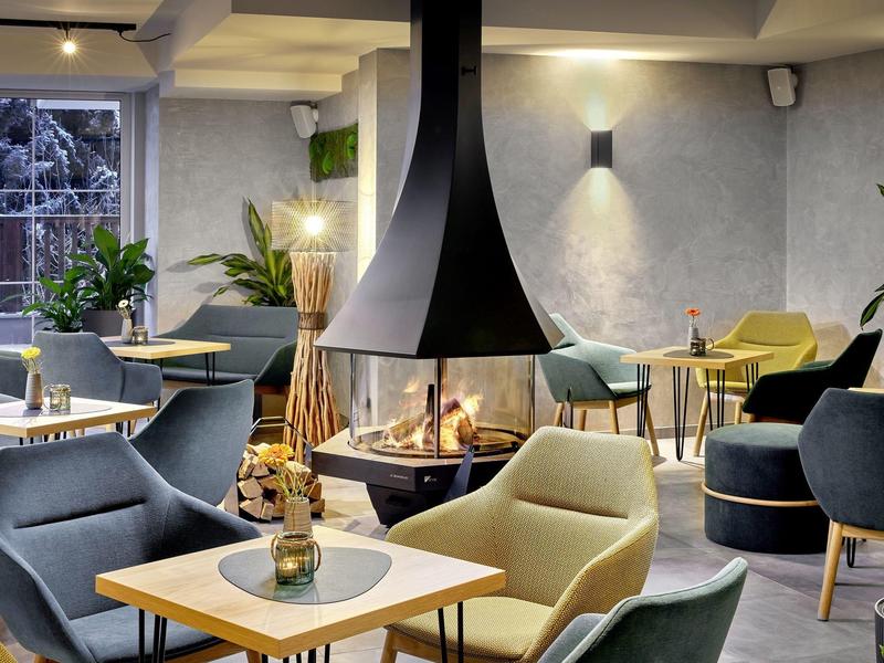 Przytulna przestrzeń hotelowa z nowoczesnymi fotelami i centralnym kominkiem.