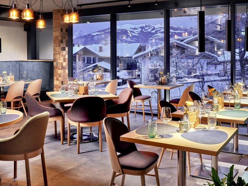 Nowoczesna restauracja z stylowymi stolikami, wygodnymi krzesłami i panoramicznym widokiem na ośnieżone góry.