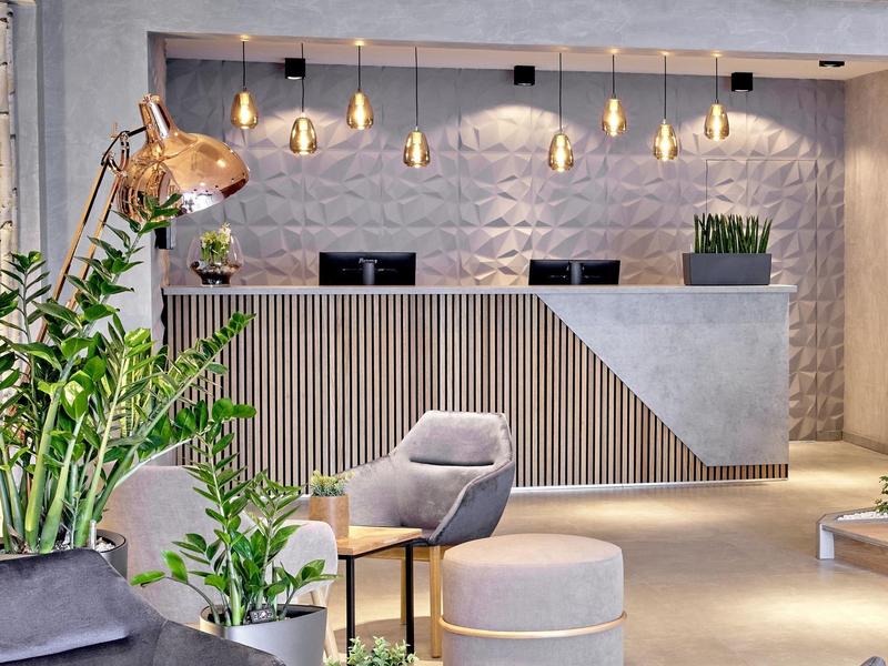Nowoczesna lobby hotelowa z recepcją, stylowymi fotelami i roślinami.