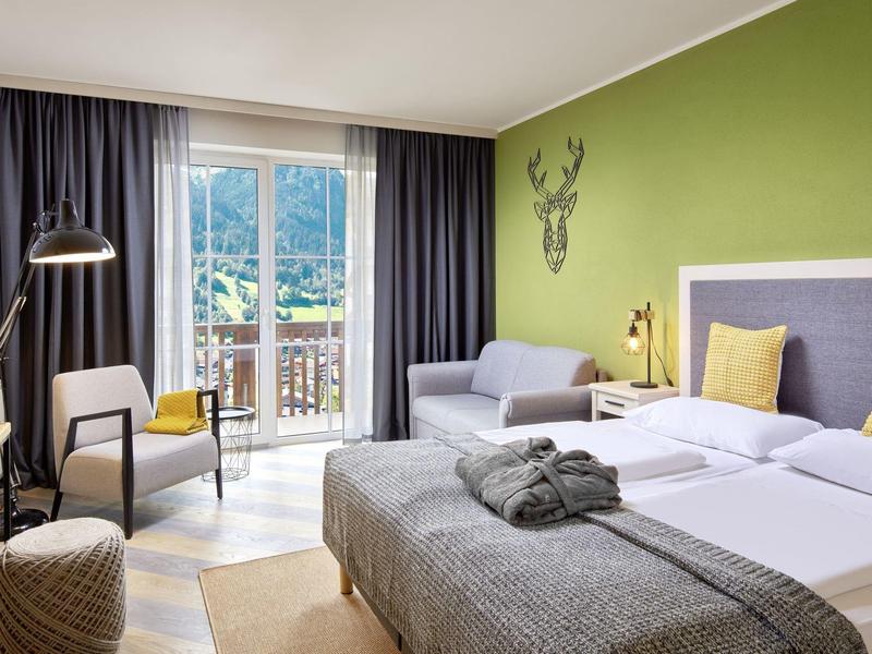 Nowoczesny pokój hotelowy z balkonem, podwójnym łóżkiem, sofą i widokiem na góry