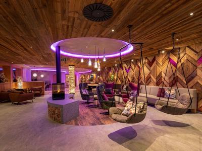 Modern hotel lounge area with hanging chairs and purple ceiling lighting.
