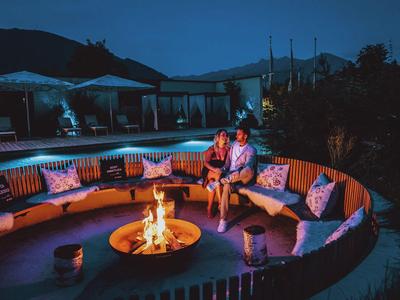 Couple sits relaxed by a fire pit in a circular outdoor seating area at night.